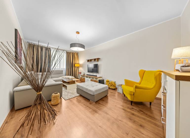 A bright living room in a three-room apartment with wood-patterned flooring and a yellow armchair.