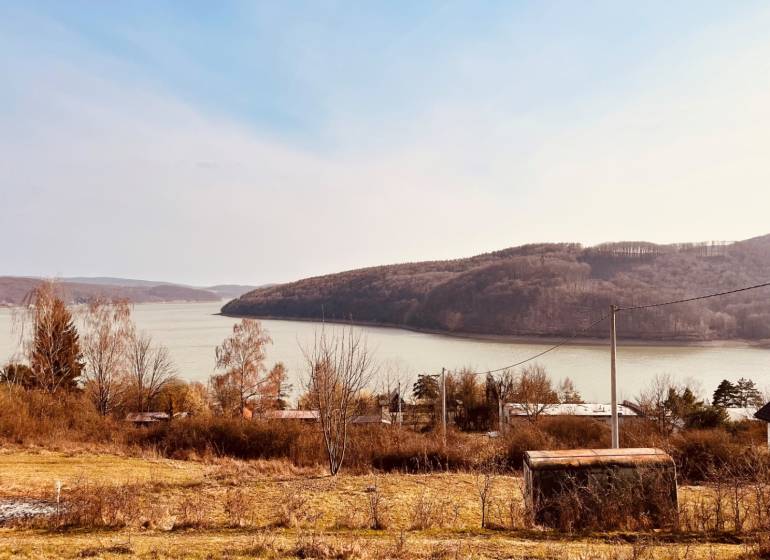 View of recreational plots in Nová Kelča near the water and wooded hills.
