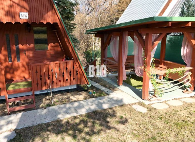 A wooden cottage in Martin next to a gazebo with pink curtains on a grassy area.