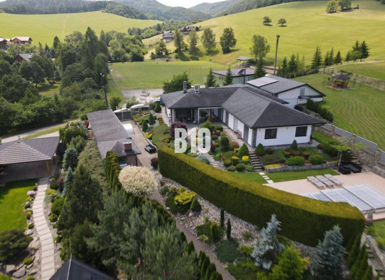 A villa in Súľov-Hradná surrounded by a beautiful garden and hilly landscape.