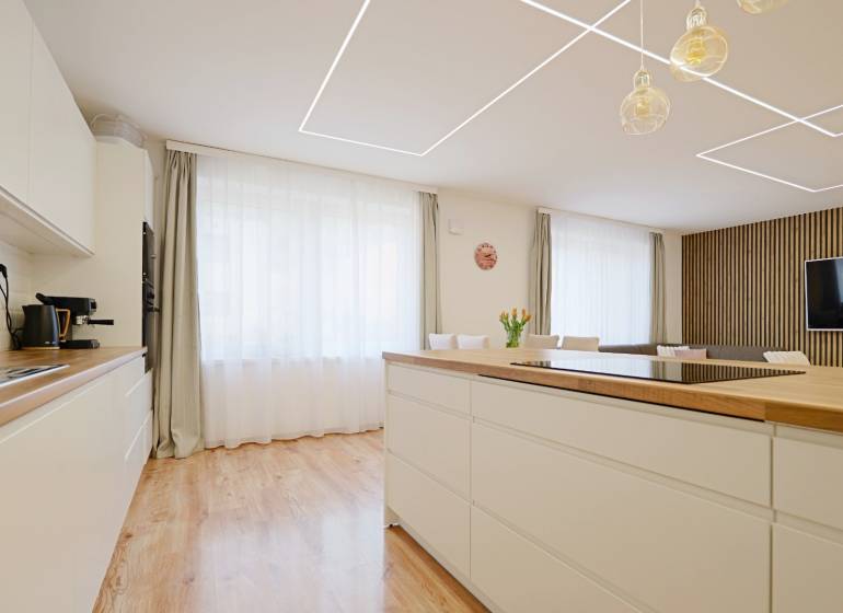 A kitchen in a family house with a wooden decor floor, light furniture, and a large window.