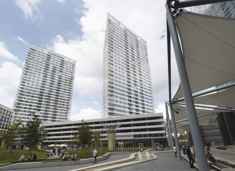High-rise buildings in the area on Landererova Street, people relaxing by the fountain and trees.