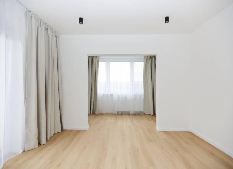 A room in a 3-room apartment with a wooden decor floor and large windows with curtains.