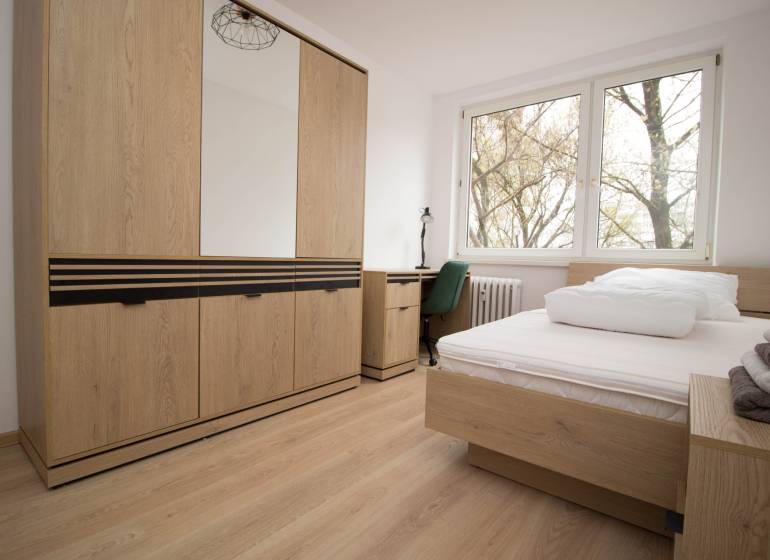 Bedroom in a 3-room apartment with a bed, wardrobe, and floor with wooden decor.