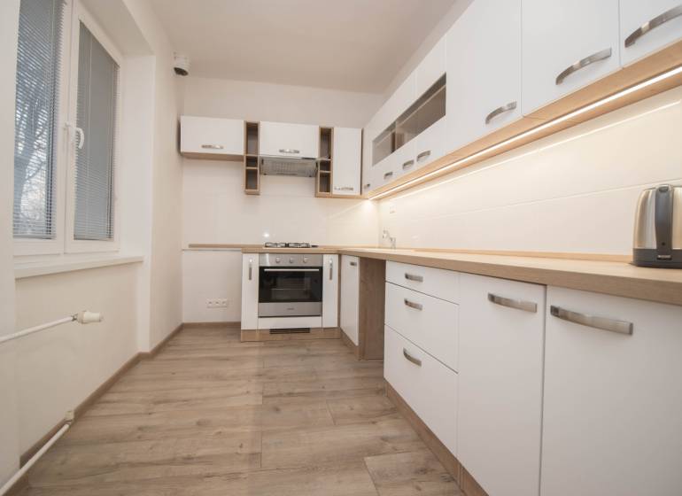 A kitchen with appliances, white cabinets, and a wood-patterned floor in a two-room apartment.