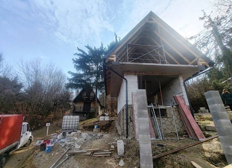 A cottage construction on Zajačia debra in Holčíkovce surrounded by trees and building materials.