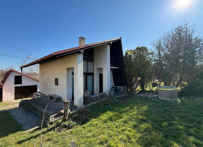 A cottage in Zlaté Moravce surrounded by a garden and lawn under a clear sky.