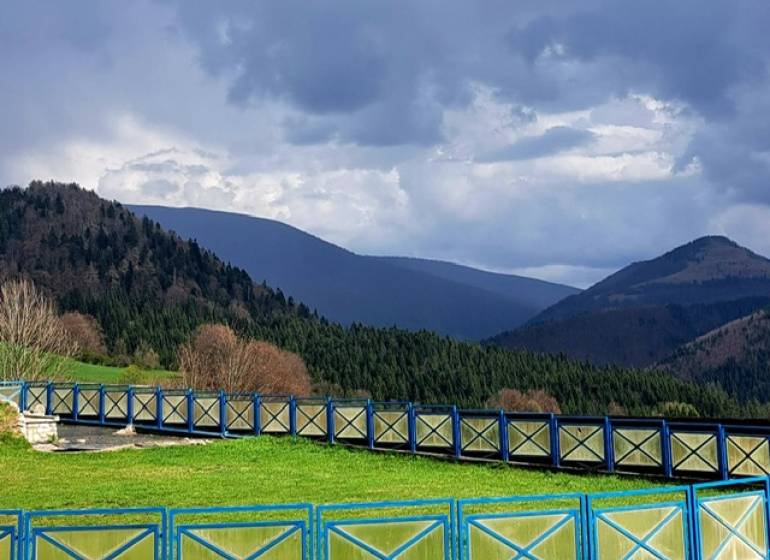 Mountain scenery in Donovaly with a blue wooden fence and forests in the background.