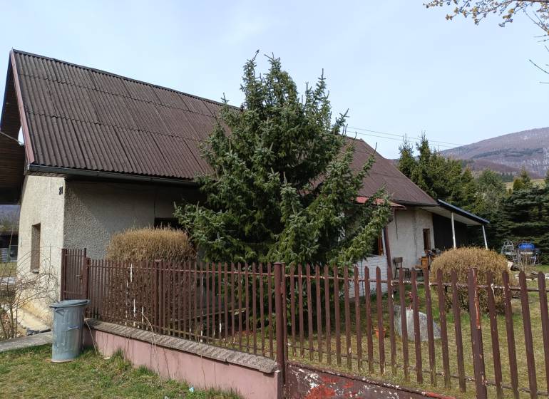A family house in Vrícko with a fenced garden near a coniferous tree.