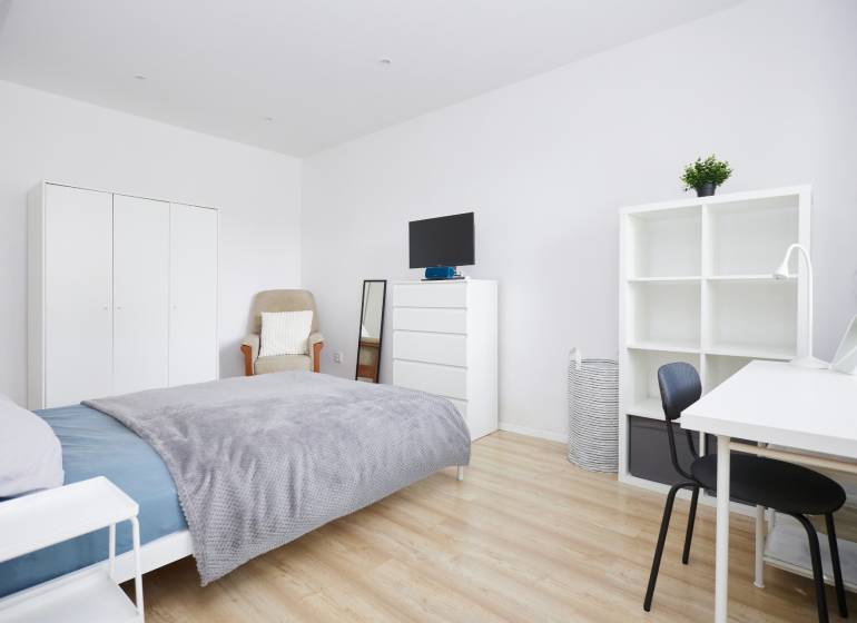 Bedroom in a 2-room apartment with white furniture and a wood-patterned floor.