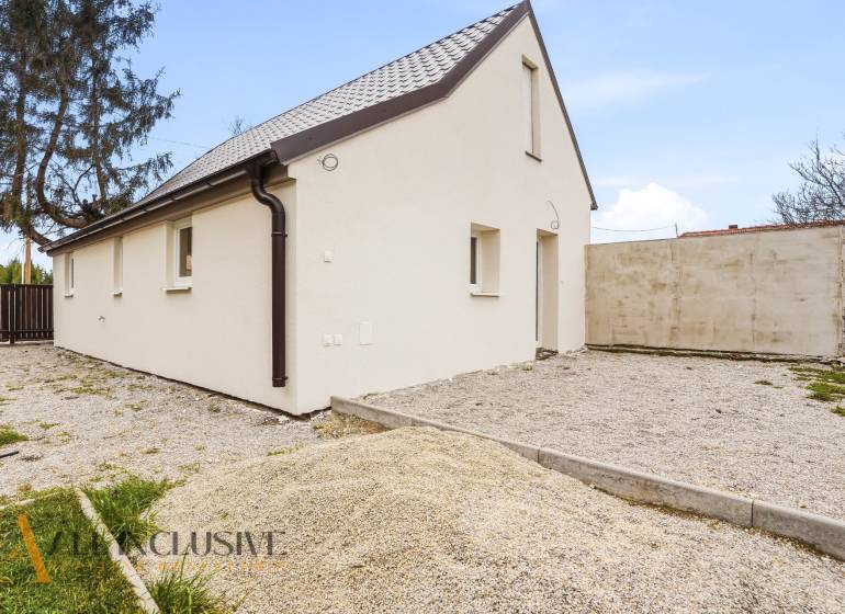 A family house in Dolný Bar with a white facade and a sloped roof on a gravel plot.