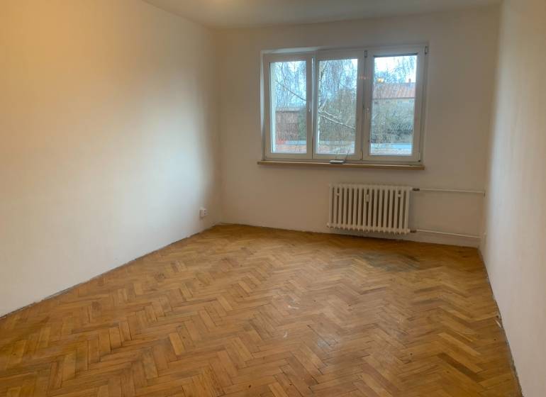 A room in a two-room apartment with a wooden decor floor and a large window.