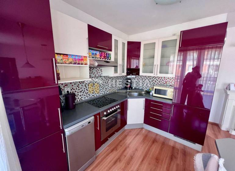 A kitchen in a studio apartment with glossy cabinets and mosaic on the wall.