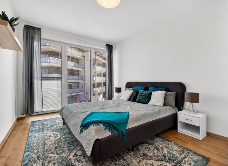A bedroom with a large bed, balcony doors, and a wooden decor floor in a 2-room apartment.