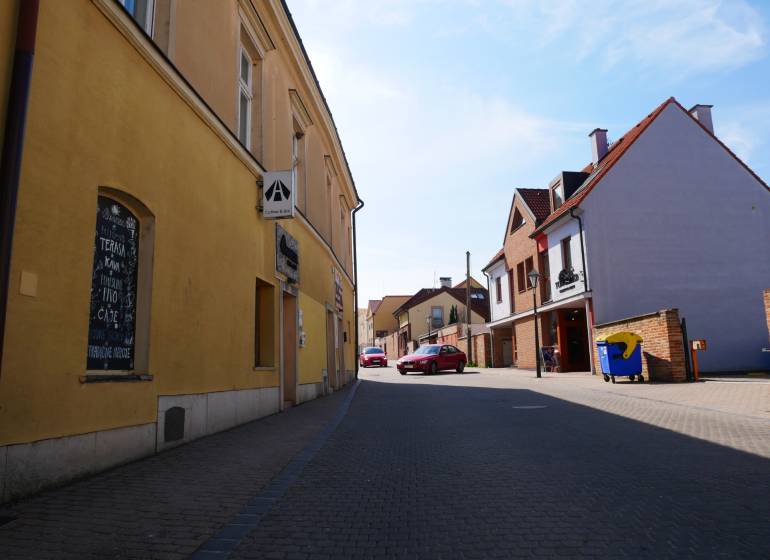 A street in Trnava with dining spaces, yellow and brick buildings, parked car.