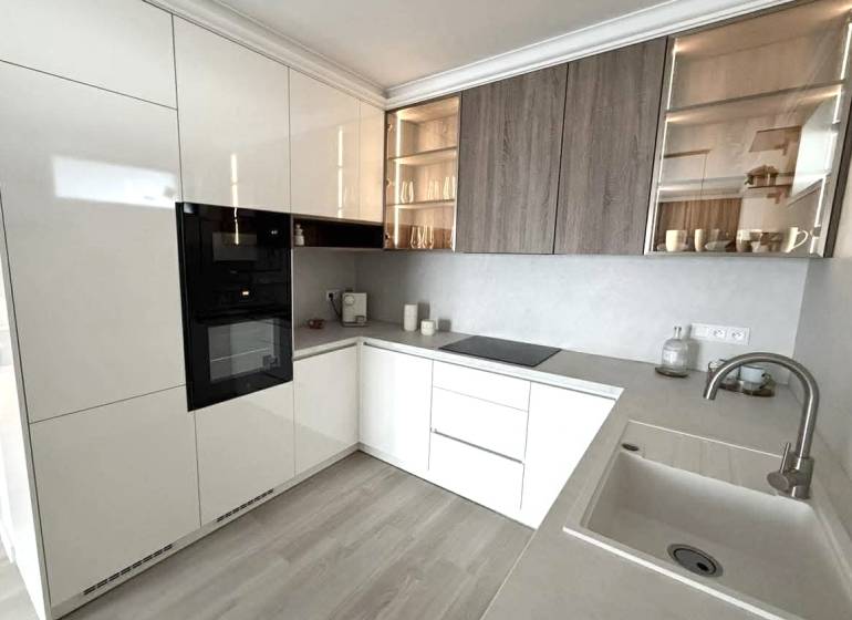 A kitchen in a 2-room apartment with white cabinets and a wooden decor floor.