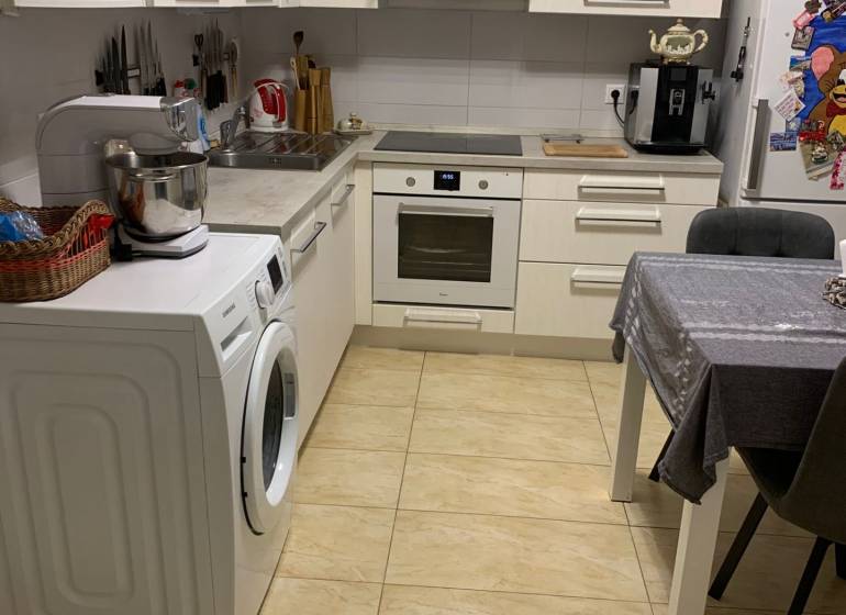 A kitchen in a 2-room apartment with white cabinets and ceramic flooring.