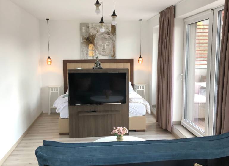 Living room in a two-room apartment with a wooden decor floor and a separate bedroom area.