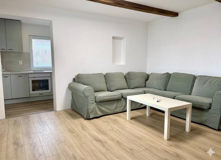 Living room with a corner sofa, wood-patterned flooring, and a kitchen in a family house.