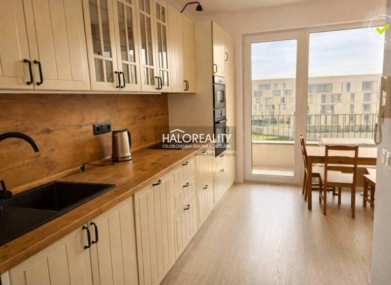 A kitchen with a wood-patterned floor, white cabinets, and a dining table in a two-room apartment.