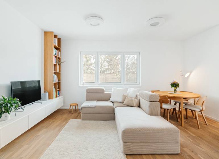 Living room with a sofa, TV, bookshelf, and dining table, floor with wooden decor.