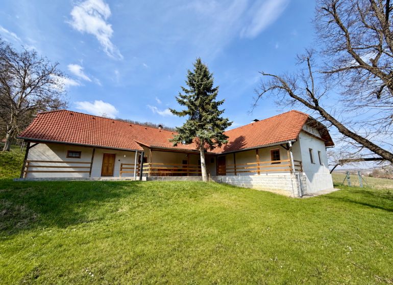 A family house in Podbranč with a red roof surrounded by greenery and trees.