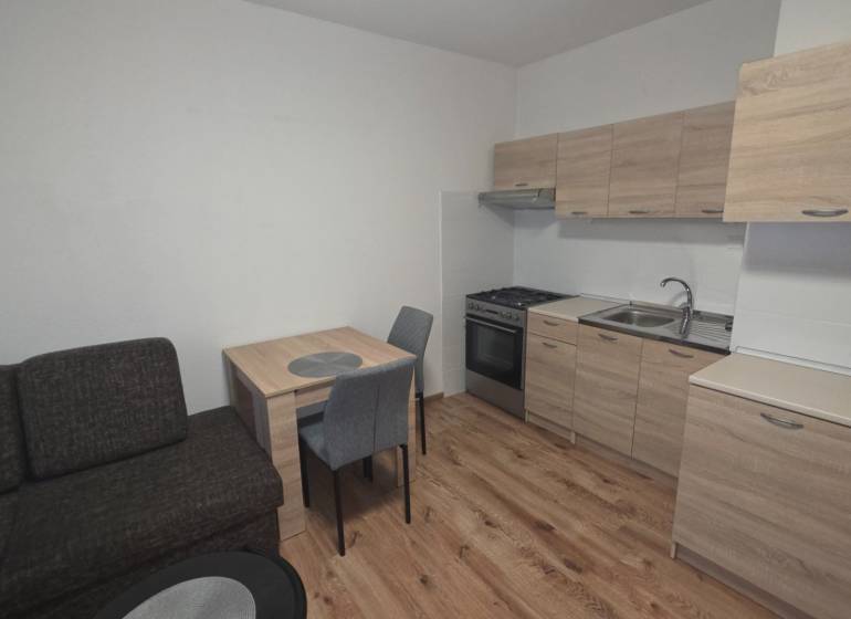 A kitchen in a studio apartment with wooden decor flooring and furniture.