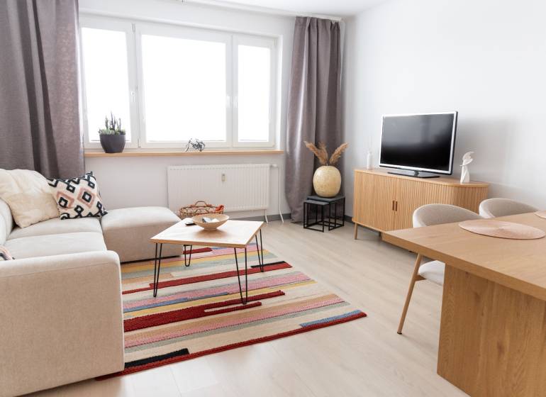 Living room in a 4-room apartment with a wooden decor floor, a sofa, and a television.