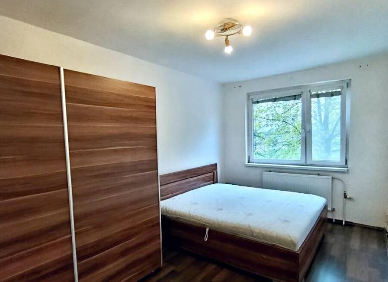 A bedroom with a wardrobe, bed, and wooden decor flooring in a 4-room apartment.