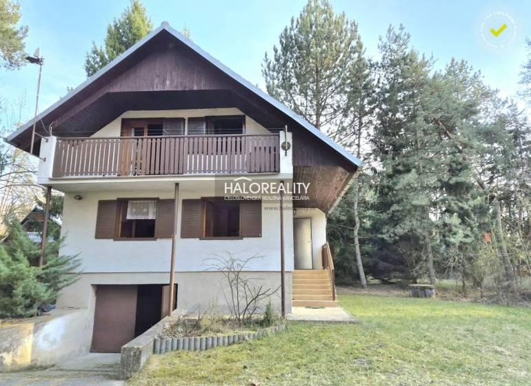 A cottage in Borský Svätý Jur surrounded by greenery and trees, with a wooden balcony.