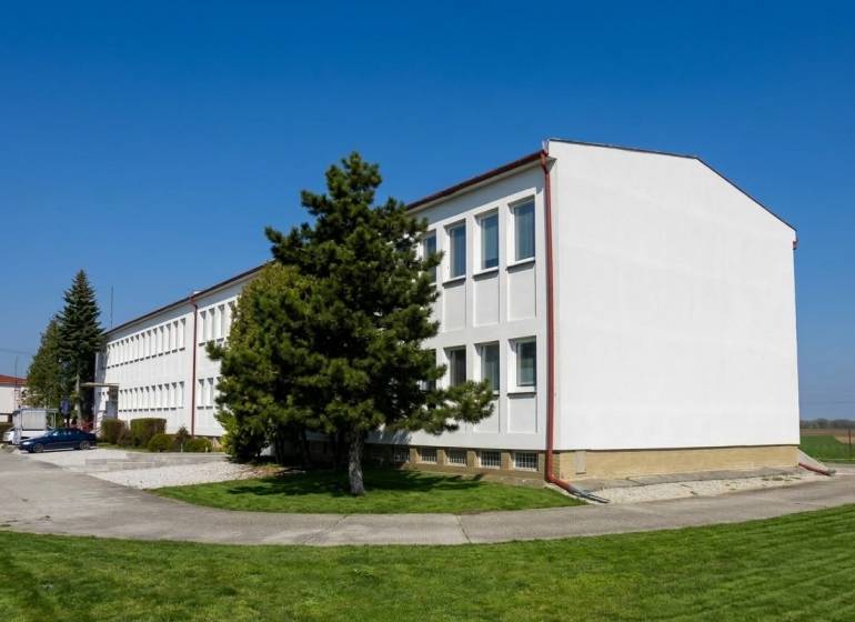 A building in Šoporňa surrounded by greenery and trees, with a clear blue sky.