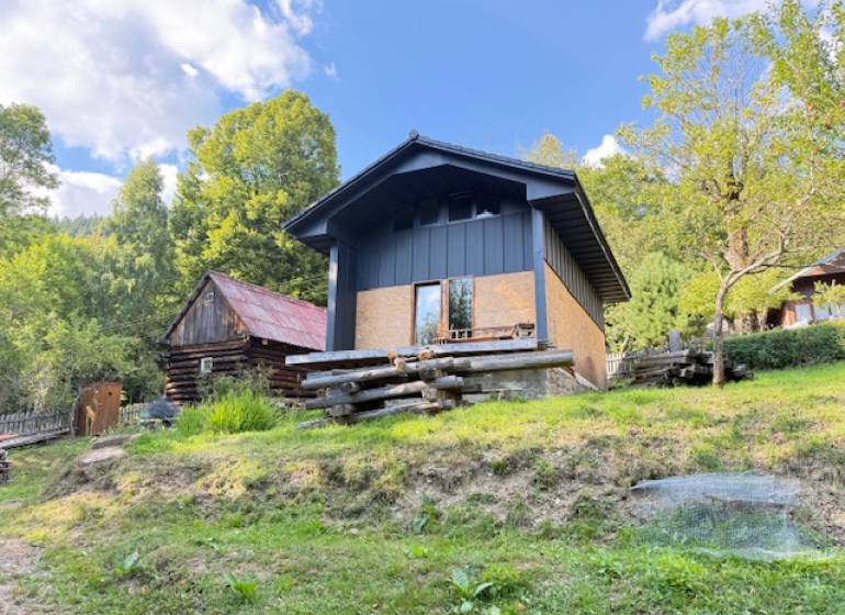 A cottage in Horná Mariková, surrounded by nature and wooden structures, on a sunny day.