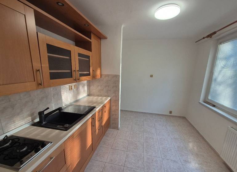 A kitchen in a studio apartment with light cabinets and ceramic tiles.