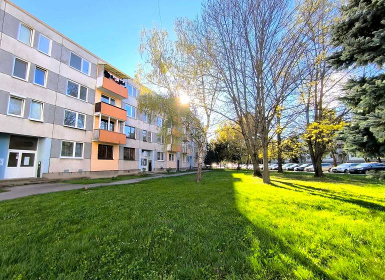 The apartment building on Veľká Okružná in Partizánske surrounded by greenery and parked cars.