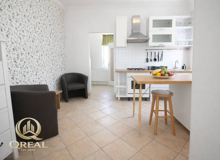 A kitchen with a bar counter, fruit, and chairs in a studio apartment.