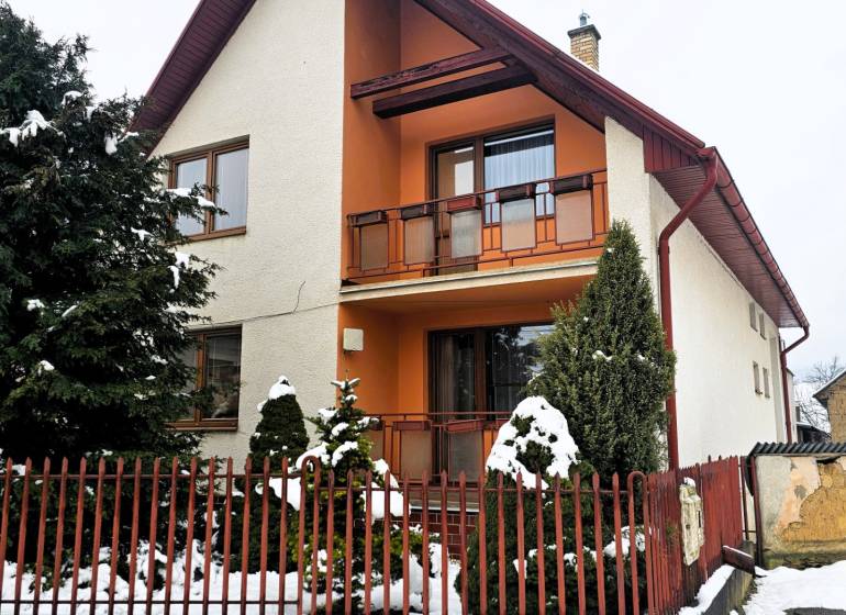 A family house in Kameňany with a snowy yard and a red fence.