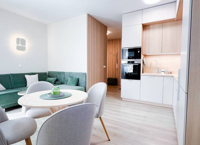 Living room and kitchen in a 3-room apartment with a wooden decor floor and a green sofa.