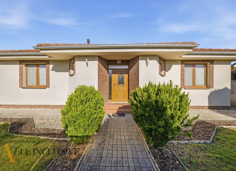 A family house in Kútniky with shrubbery, a white facade, and brown accents.