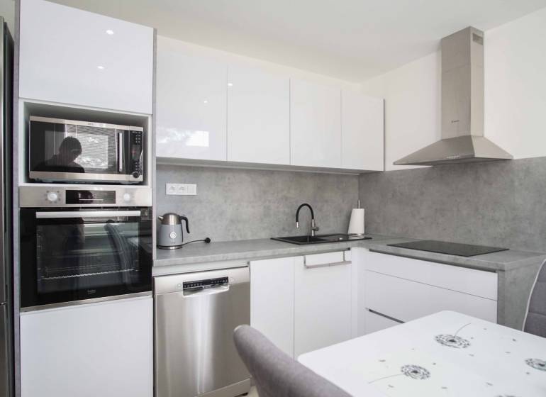 A modern kitchen with white cabinets in a 2-room apartment, equipped with appliances and a range hood.