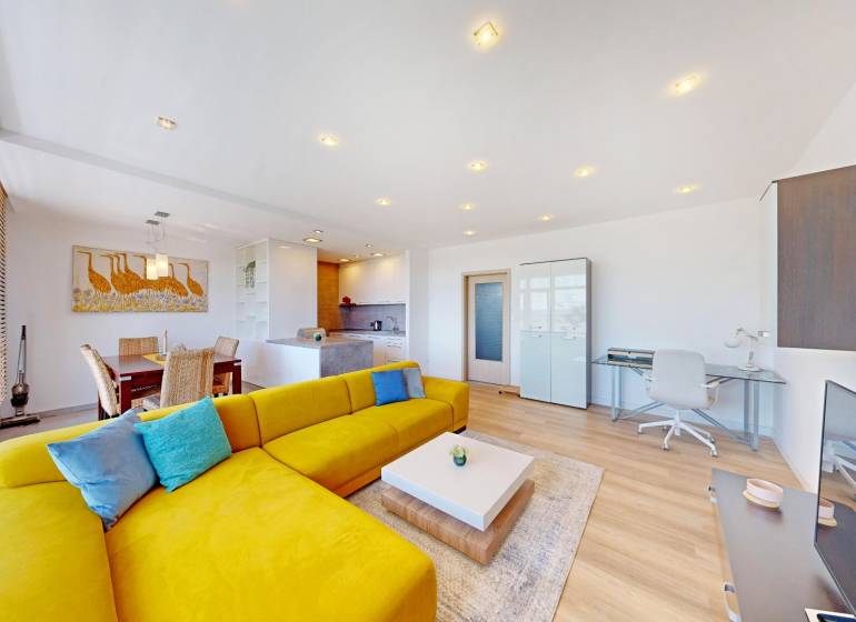 A bright living space with a striking yellow sofa, dining area, and wood-patterned flooring.