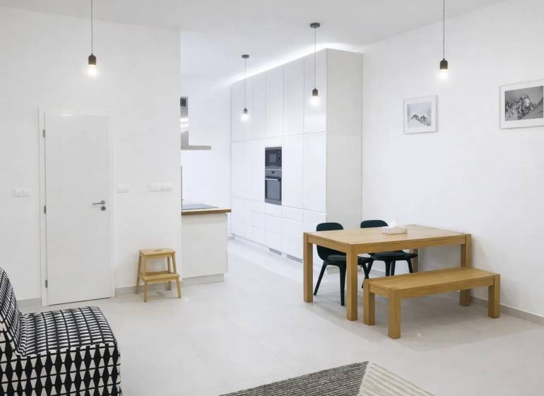 Interior of a 2-room apartment with white walls, a wooden table, and a black sofa.