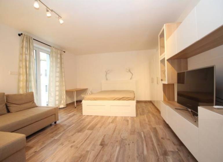 Living area in a studio apartment with a bed and a floor with a wood decor.