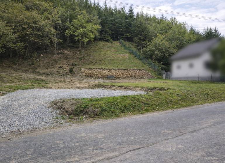 A sloped plot of land in the village of Makov with an access road and surrounding forest vegetation. Land - residential.