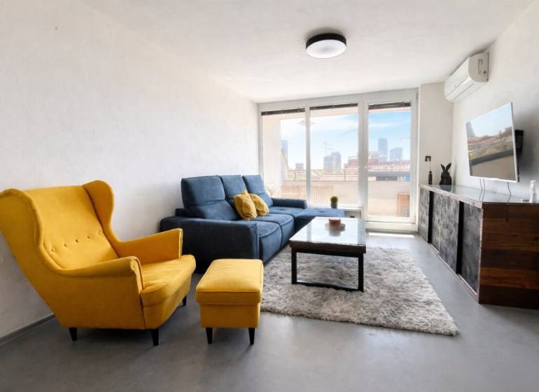 Living room in a 3-room apartment with a yellow armchair, a blue sofa, and a TV on the wall.
