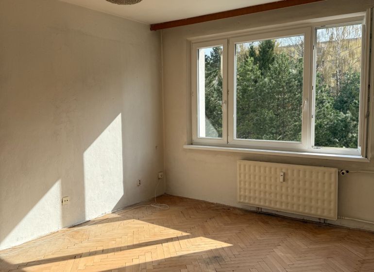 A room with a large window, a chandelier, and a floor with a wooden decor, a 2-room apartment.