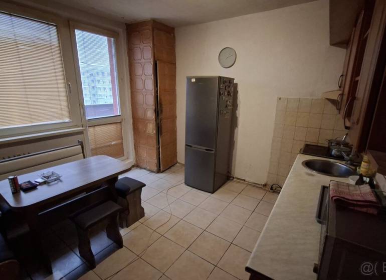 A kitchen in a 3-room apartment with tiles and simple furniture, a refrigerator, and a dining table.