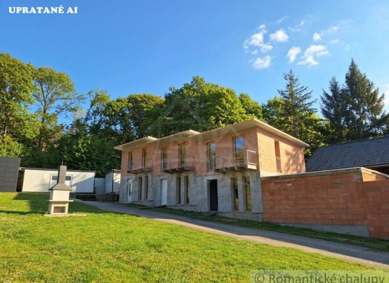 A two-story unfinished cottage in Divín surrounded by greenery and a grassy plot.