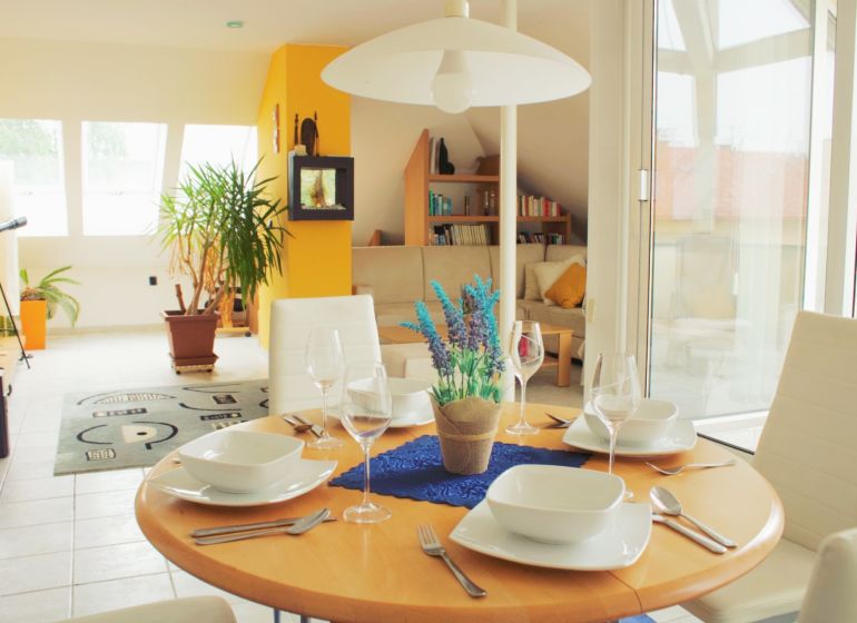 Interior of a holiday apartment with a dining table, plants, and a view of the living area.