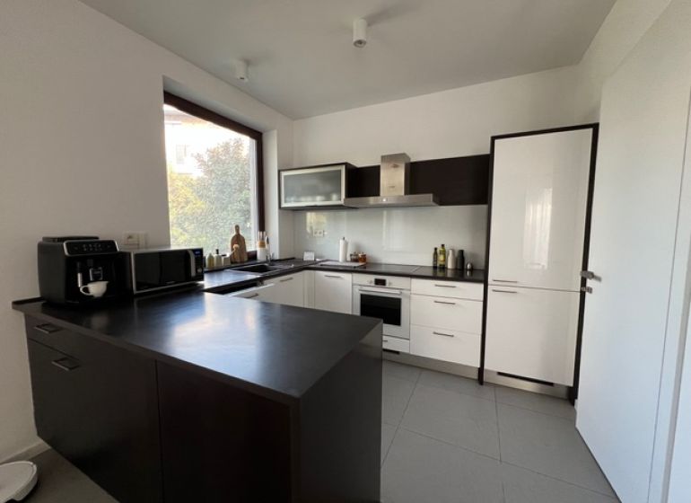 A modern kitchen with a dark countertop in a two-room apartment, equipped with appliances and a large window.