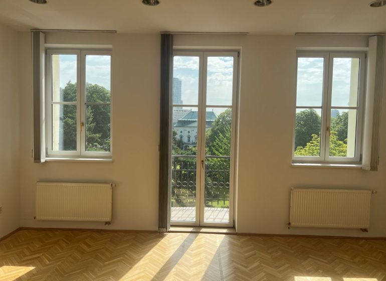 An empty room with parquet flooring, large windows, and a view of Štefánikova Street, suitable for offices.